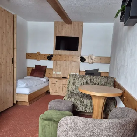 Gemütlicher Raum mit zwei Sessel, Fernseher und einem Bett.