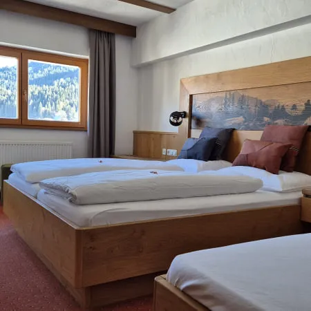 Zimmer mit zwei Betten, Holzmöbeln und Fenstern mit Bergblick