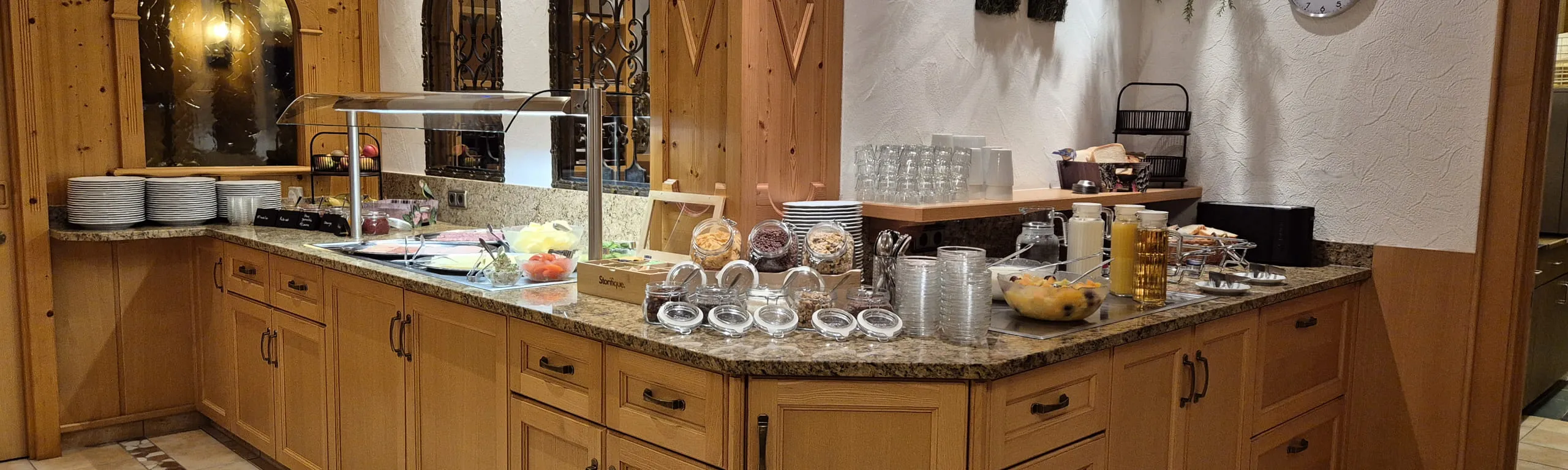 Frühstücksbuffet mit Brötchen, Obst und Getränken auf einem Holztresen