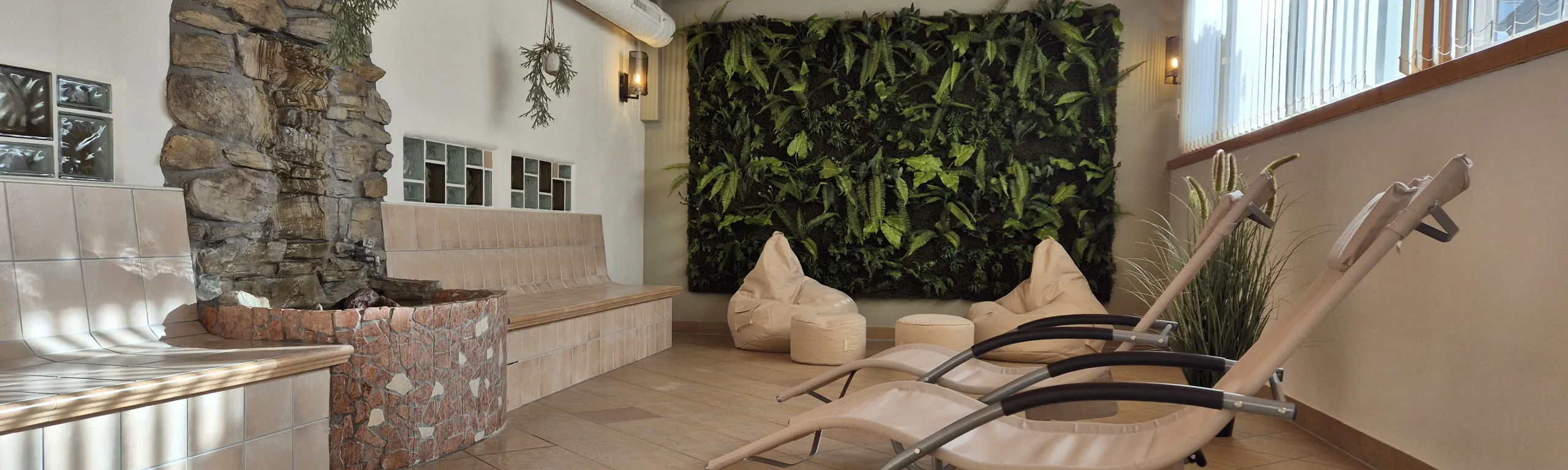 Saunalandschaft mit Liegen, Steinmauer und Pflanzenwand.