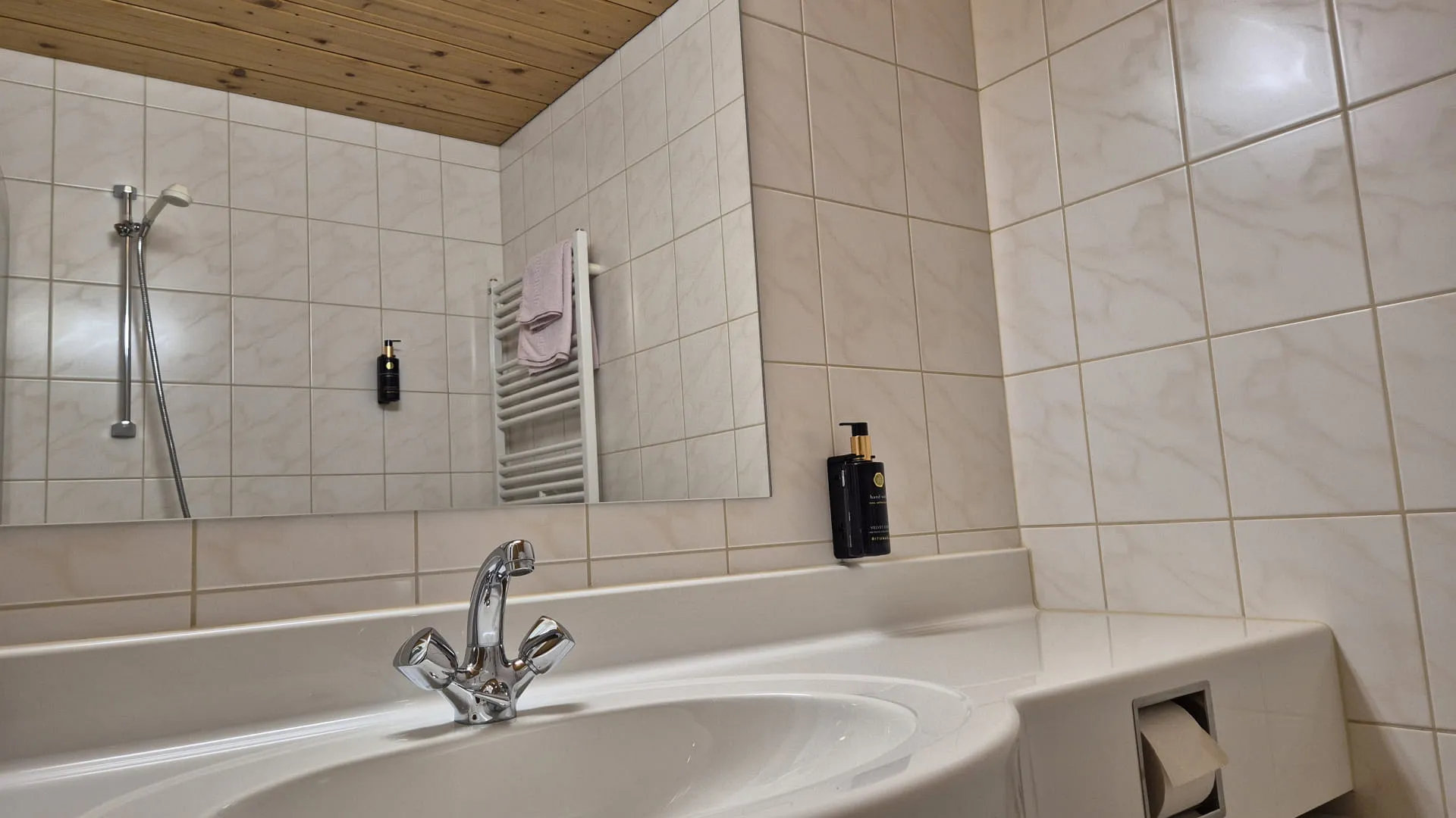 Wastafel met kraan en spiegel, betegelde muren, houten plafond