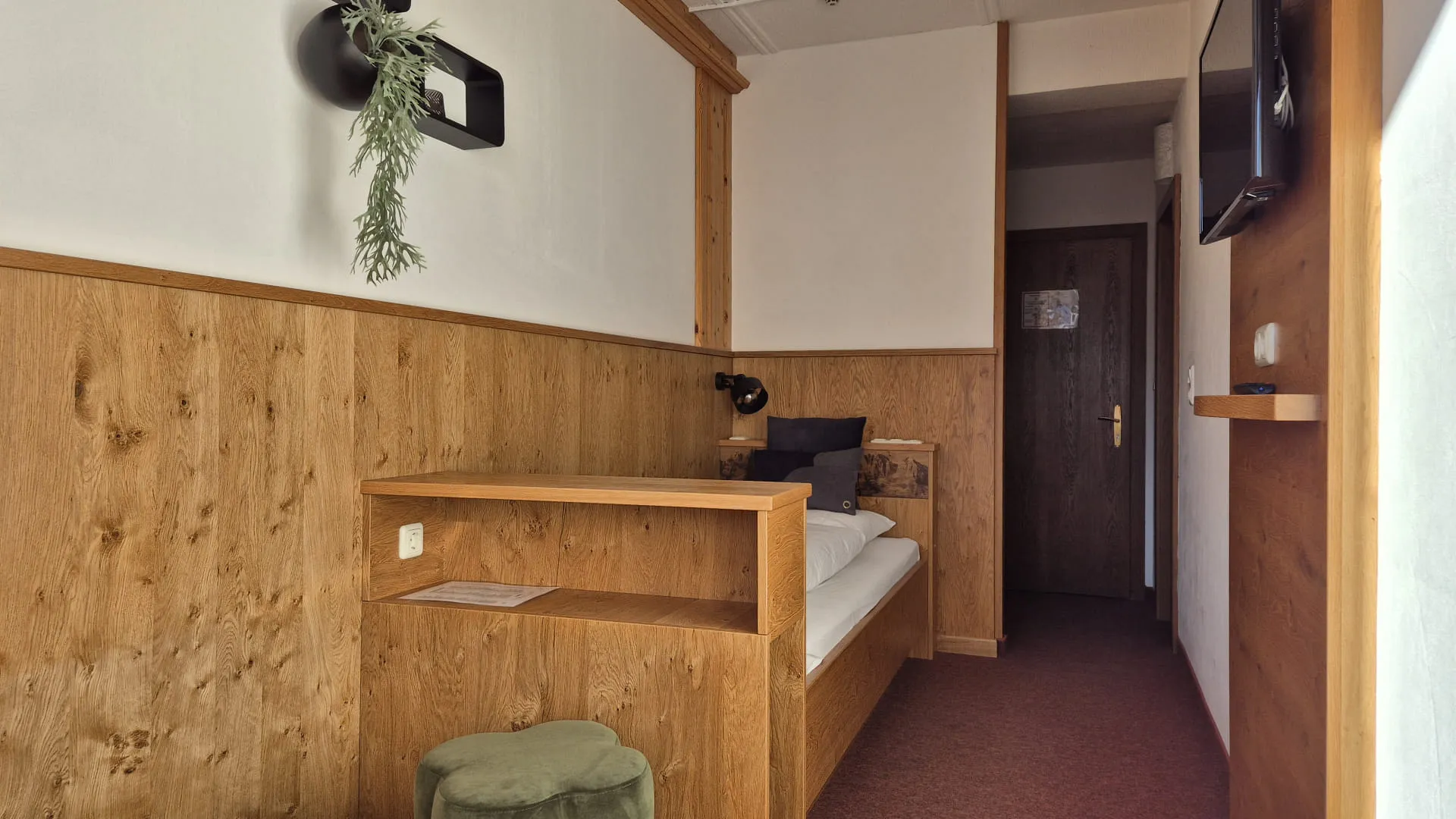 Lichte gang met houten panelen, bed, tv en plant