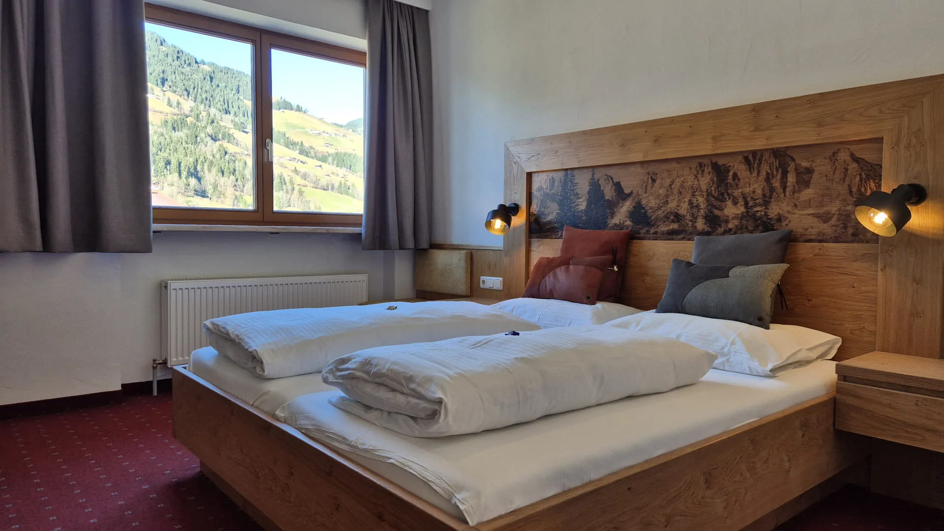 Helles Schlafzimmer mit Fensterblick auf Berge, Holzbetten und dekorativen Kissen.