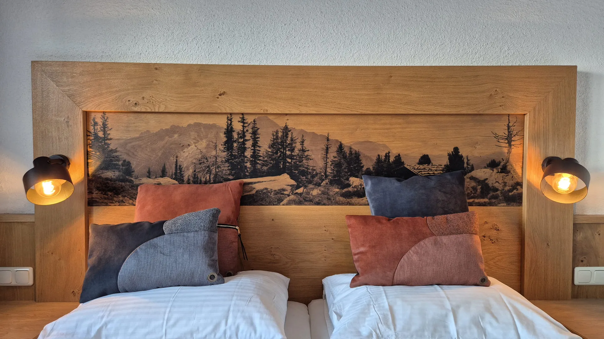 Holzkopfteil mit Bergkunstwerk und bunten Kissen auf einem Bett