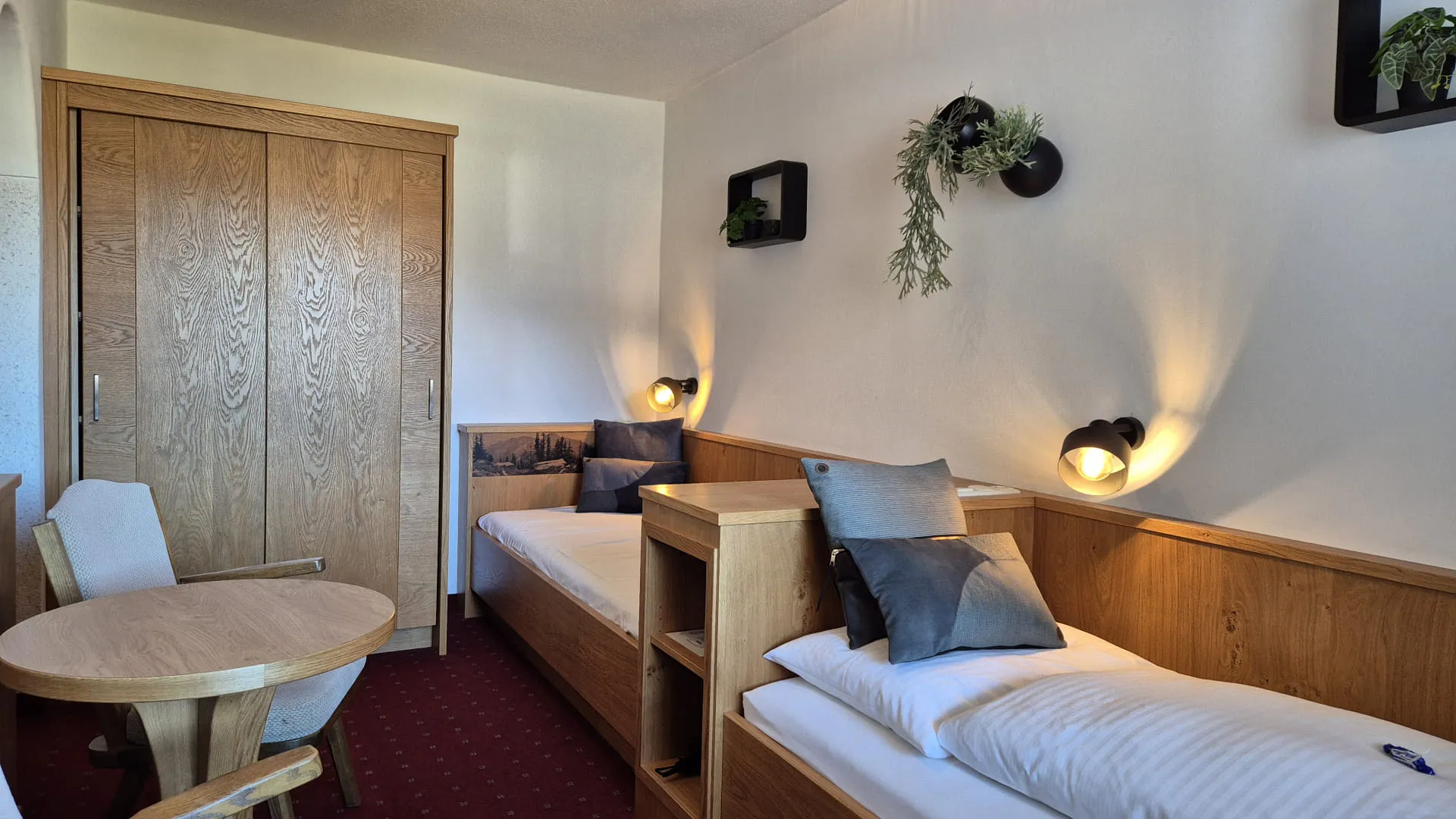 A twin room with two beds, a small table, and wall-mounted plants