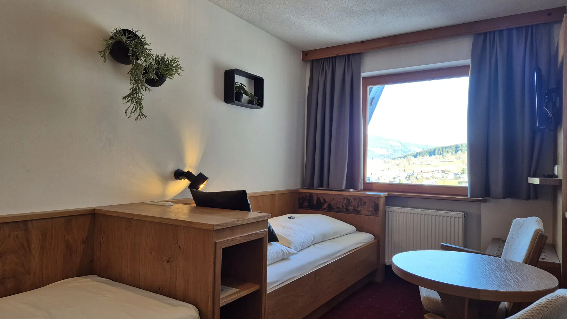 A cozy room with two beds, a table, and a large window overlooking a scenic view.